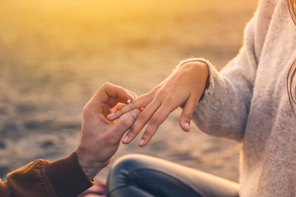A man gently places a ring on a woman's finger during a purposeful moment.